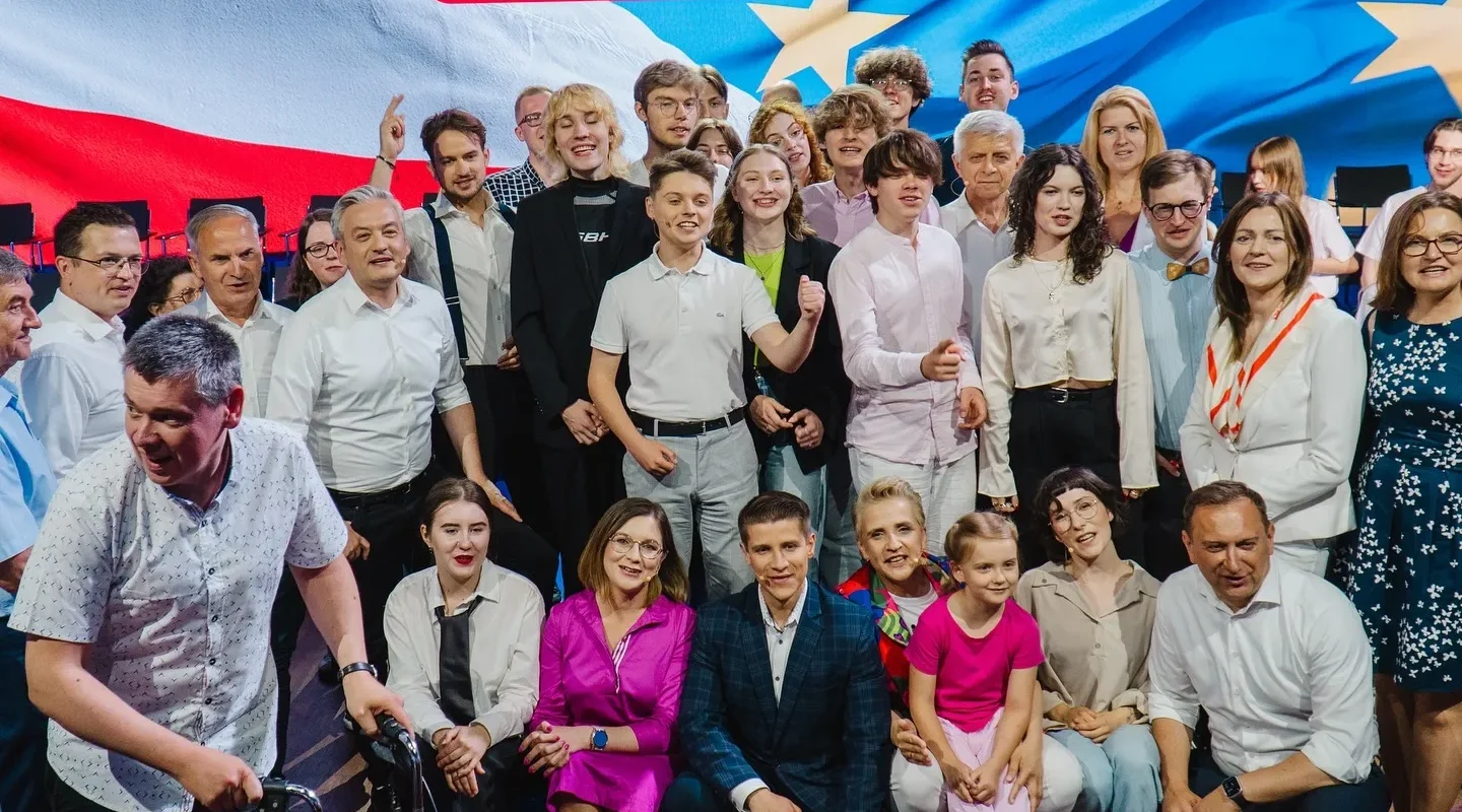 Duża grupa młodych ludzi i dorosłych stoi razem na scenie przed tłem z flagami europejskimi podczas Konwencji Europa dla Młodych.