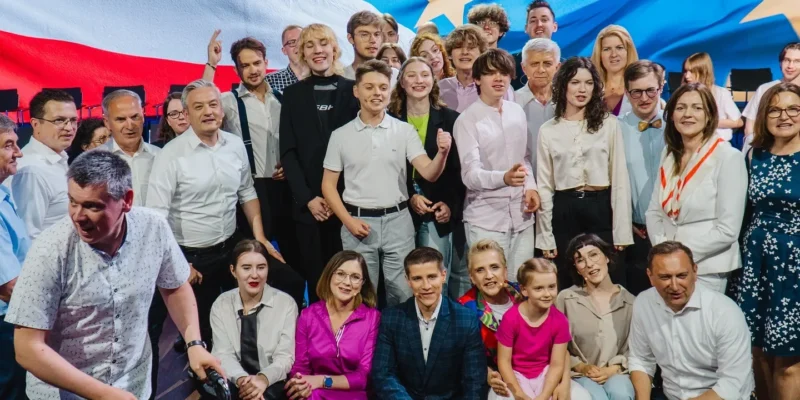 Duża grupa młodych ludzi i dorosłych stoi razem na scenie przed tłem z flagami europejskimi podczas Konwencji Europa dla Młodych.