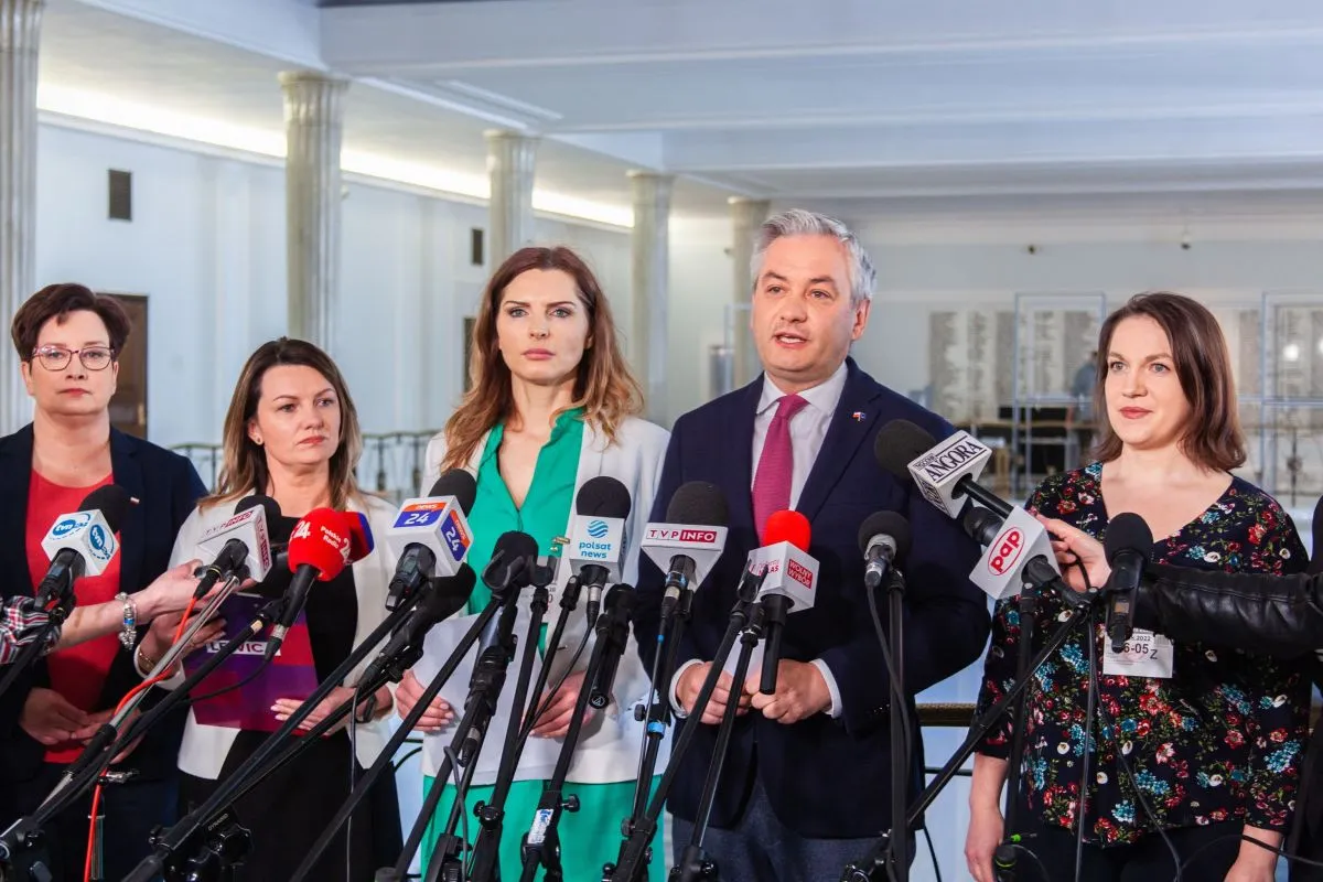 Na zdjęciu widoczni są politycy oraz dziennikarze podczas konferencji prasowej.