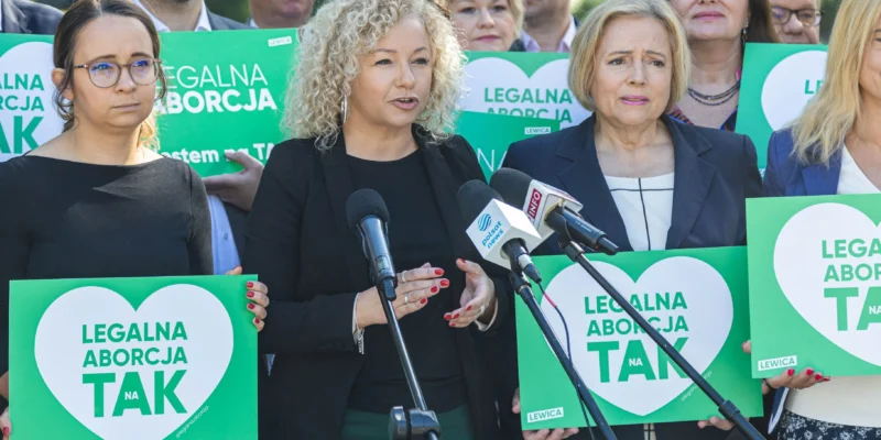 Na zdjęciu widzimy grupę osób trzymających zielone transparenty z napisem "LEGALNA ABORCJA TAK", podczas konferencji prasowej poświęconej temu tematowi.