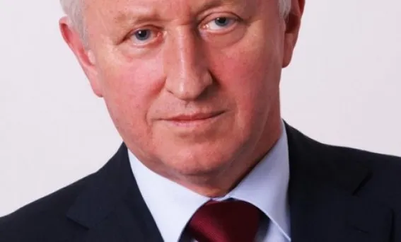 Portret starszego mężczyzny w granatowym garniturze i czerwonym krawacie, patrzącego prosto w obiektyw.