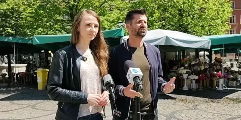 Na zdjęciu dwie osoby, mężczyzna i kobieta, stoją na tle targu, prowadząc rozmowę przy mikrofonie.