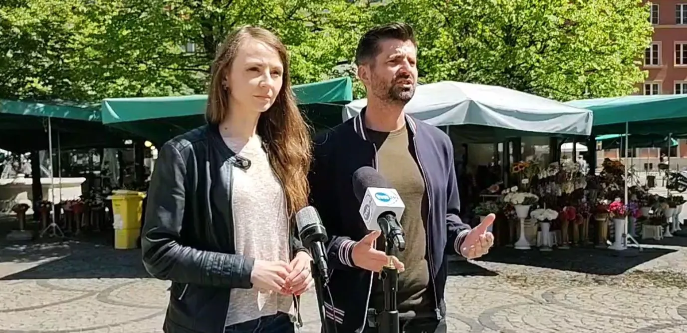 Na zdjęciu dwie osoby, mężczyzna i kobieta, stoją na tle targu, prowadząc rozmowę przy mikrofonie.