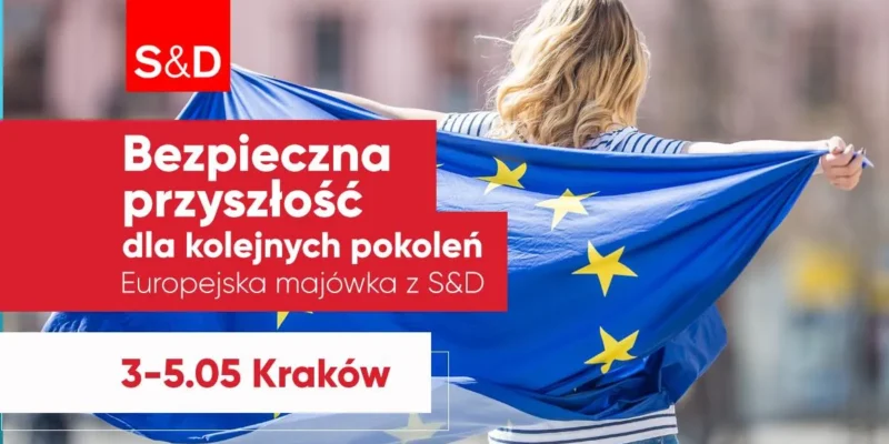 Osoba widziana od tyłu trzyma flagę Unii Europejskiej na tle czerwonego baneru promocyjnego Europejskiej majówki z S&D w Krakowie (3–5 maja).