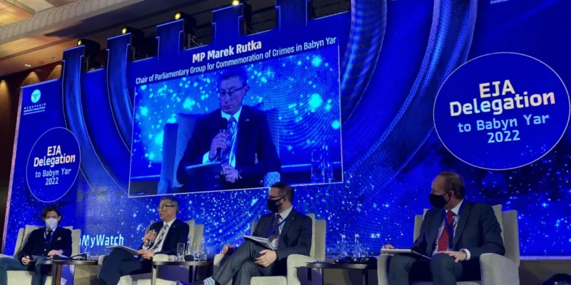 Na zdjęciu przedstawiono panel dyskusyjny z udziałem polityków w trakcie wydarzenia poświęconego upamiętnieniu zbrodni w Babim Jarze, z wyświetlonym w tle wystąpieniem posła Marka Rutki.