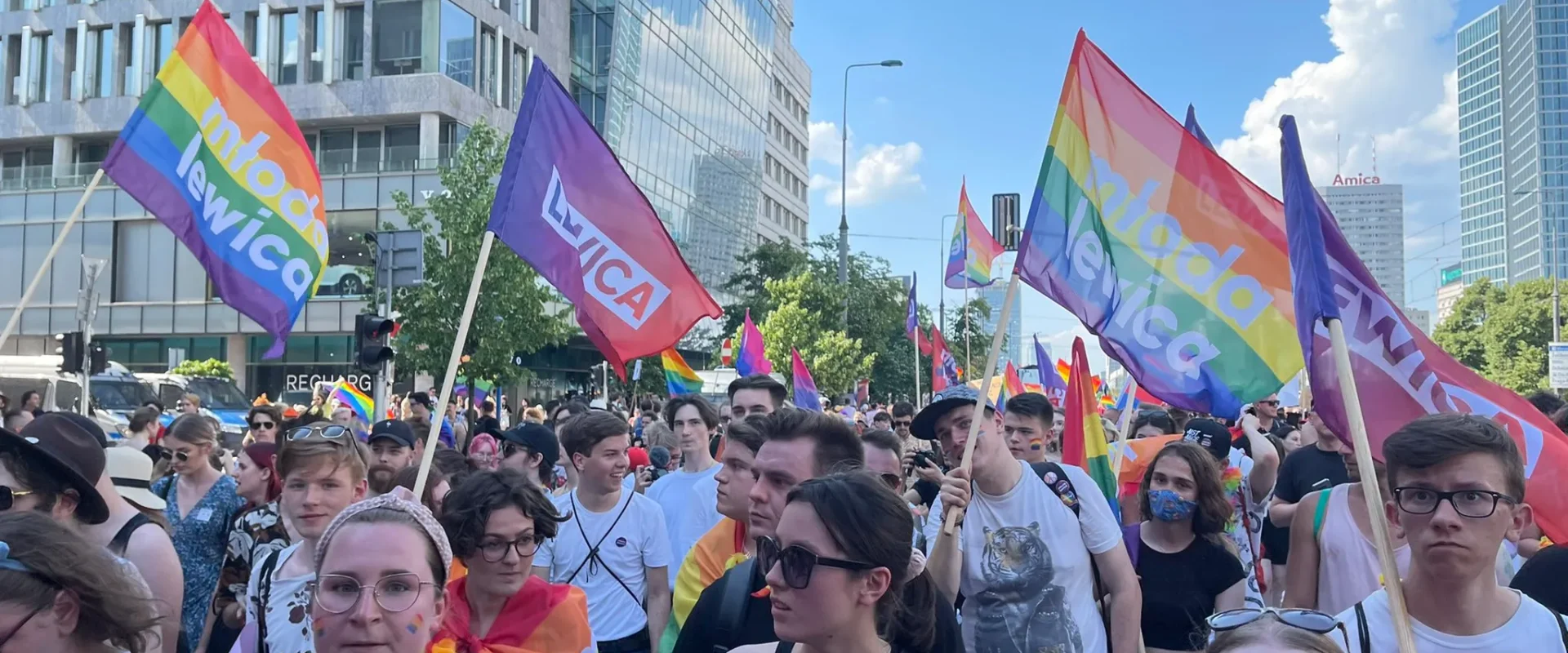 Kilkudziesięcioosobowy tłum na Paradzie Równości 2021 trzyma tęczowe flagi, w tym flagi z napisem Młoda Lewica.