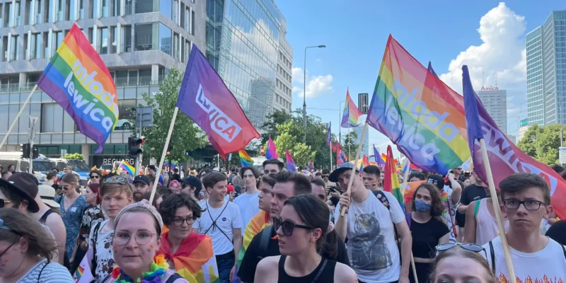 Kilkudziesięcioosobowy tłum na Paradzie Równości 2021 trzyma tęczowe flagi, w tym flagi z napisem Młoda Lewica.
