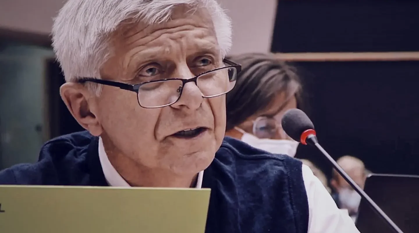 Starszy mężczyzna z siwymi włosami i okularami przemawia do mikrofonu podczas panelu konferencji.