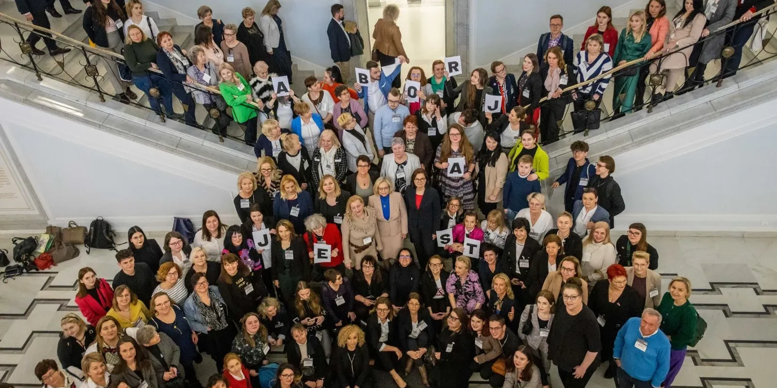 Grupa uczestników wydarzenia stoi na schodach, trzymając litery układające się w hasło „ABORCJA JEST”.