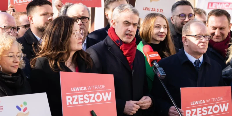 Na zdjęciu widoczna jest grupa ludzi na wiecu politycznym, trzymających czerwone plakaty z hasłem "Lewica w trasie Rzeszów".