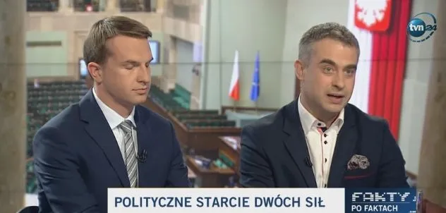 Dwaj mężczyźni w garniturach prowadzą dyskusję w studiu telewizyjnym, przed nimi pasek z napisem "POLITYCZNE STARCIE DWÓCH SIŁ", a w tle widać polskie flagi i godło.
