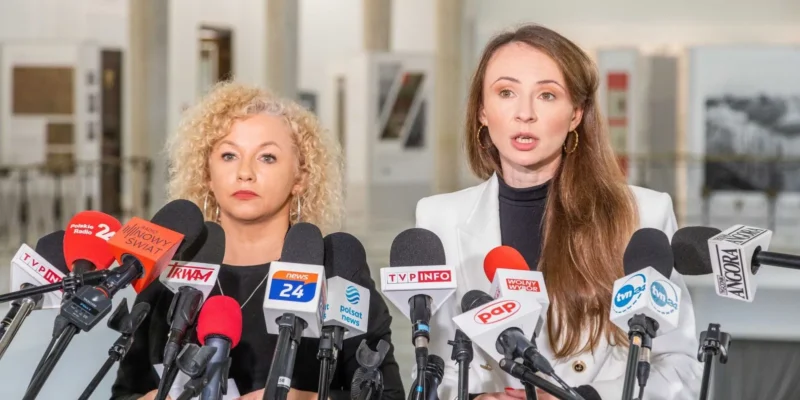 Dwie kobiety stoją przed mikrofonami w trakcie konferencji prasowej w publikuje.