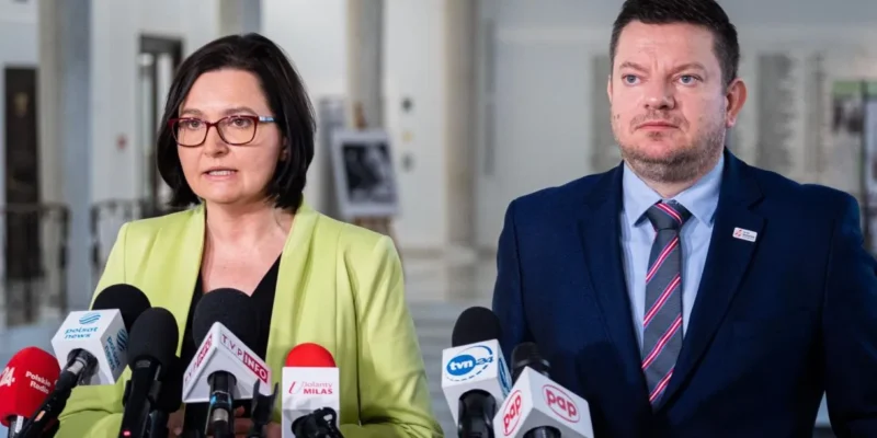 Na zdjęciu widoczna jest dwójka mówiących przy mikrofonach w budynku, najprawdopodobniej podczas konferencji prasowej.