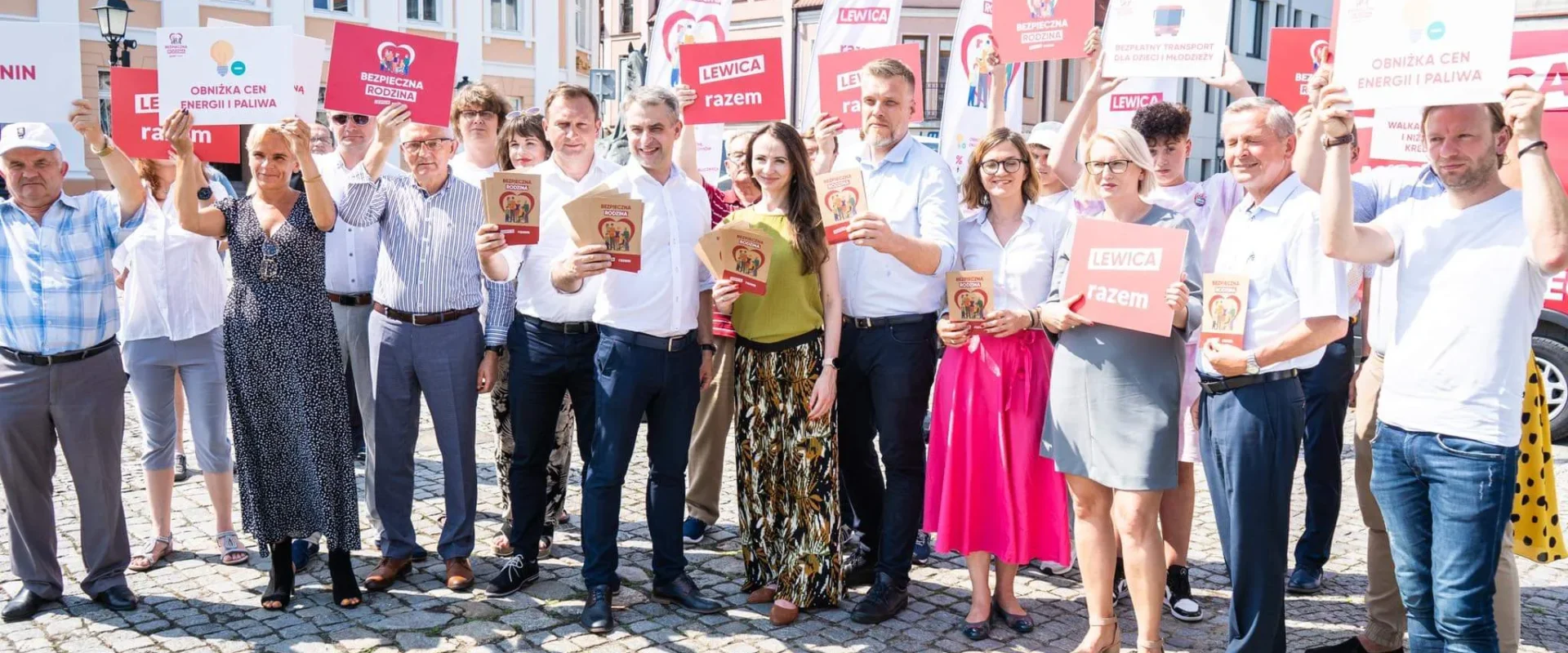 Grupa osób trzymających plakaty i ulotki na tle miasta, promująca inicjatywy społeczne i polityczne.