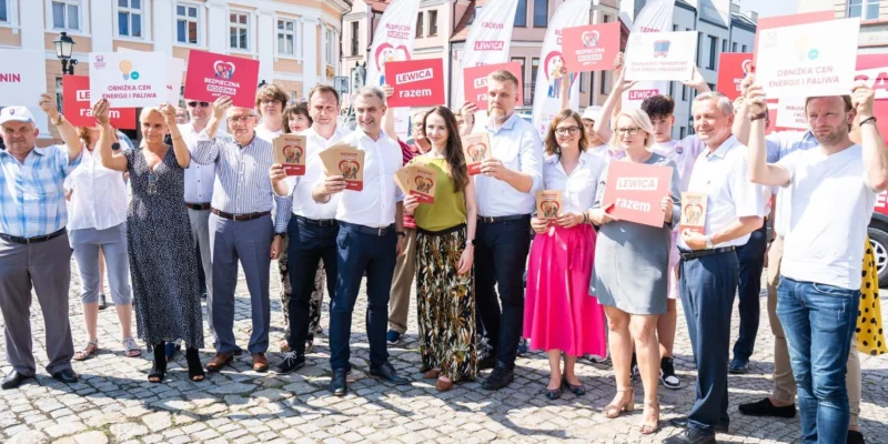 Grupa osób trzymających plakaty i ulotki na tle miasta, promująca inicjatywy społeczne i polityczne.