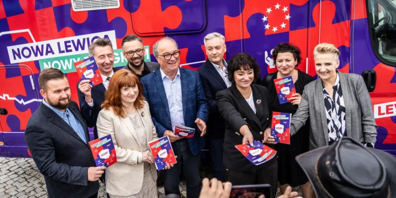 Grupa osób stojących obok kolorowego kampera kampanii Nowa Lewica, trzymających plakaty i broszury promujące konsultacje programowe.