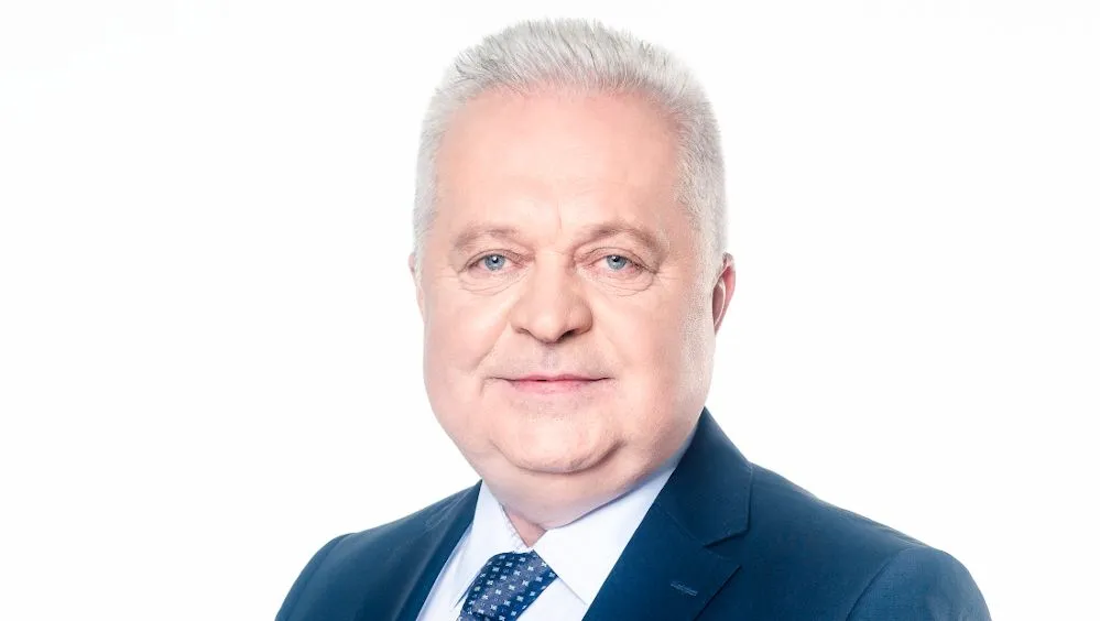 Portret mężczyzny w granatowym garniturze, białej koszuli i granatowym krawacie na białym tle.