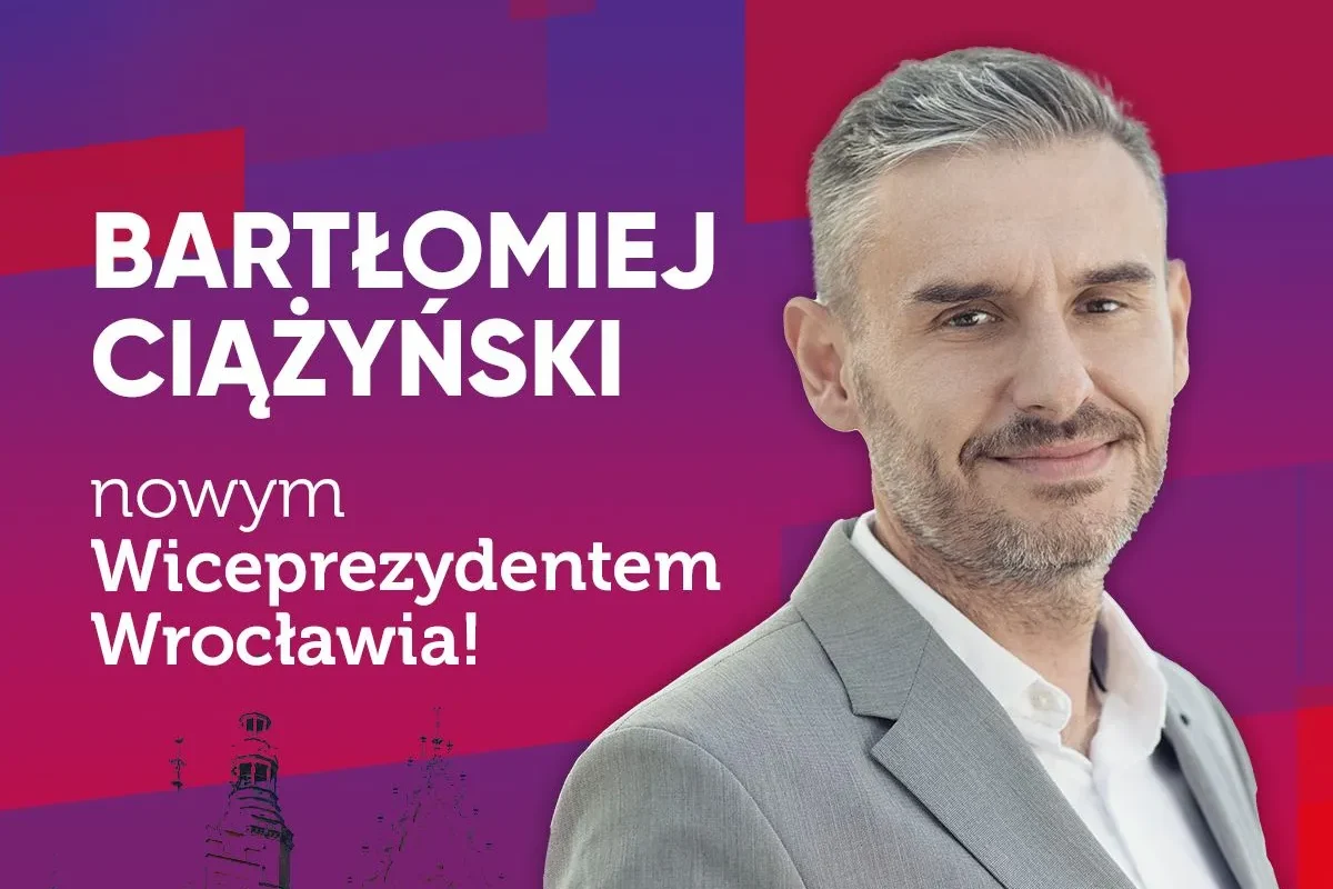 Plakat wyborczy z mężczyzną w szarym garniturze na gradientowym tle w odcieniach fioletu i różu, z dużym napisem informującym o nowym wiceprezydencie Wrocławia.