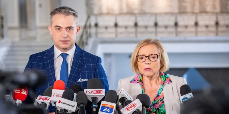 Dwóch polityków Lewicy stoi przy licznych mikrofonach podczas konferencji prasowej.