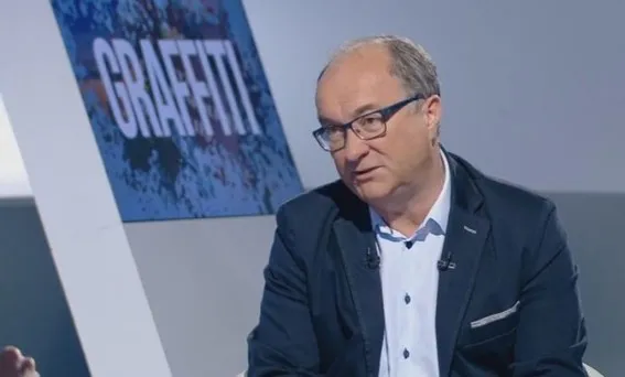 Mężczyzna w okularach i marynarce siedzi w studiu telewizyjnym podczas rozmowy o miesięcznicach smoleńskich.