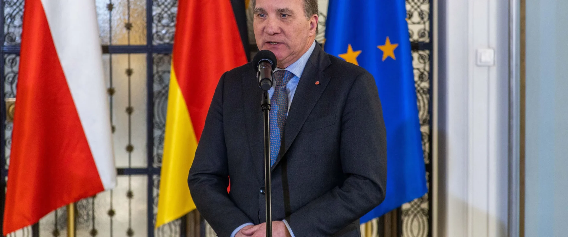 Na zdjęciu widać mężczyznę przemawiającego do mikrofonu, stojącego przed flagami Polski, Niemiec oraz Unii Europejskiej.