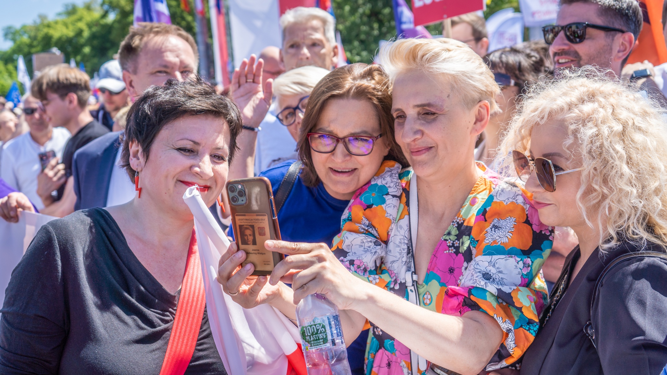 Grupa kobiet na Marszu Lewicy 4 czerwca robi wspólne selfie telefonem wśród tłumu z kolorowymi ubraniami i flagami.