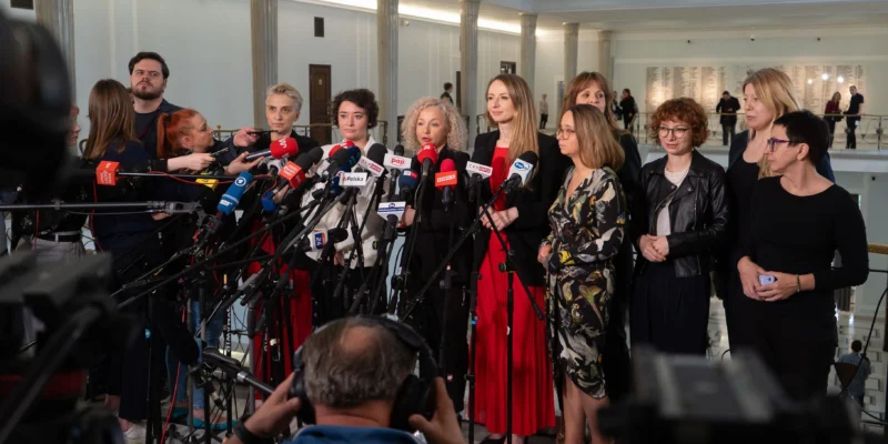 Grupa polityków Lewicy podczas konferencji prasowej w Sejmie, otoczona mikrofonami i kamerami dziennikarzy.