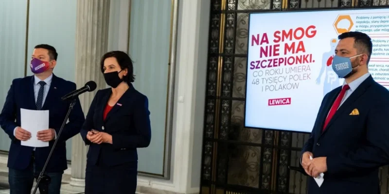 Trzy osoby w garniturach i maseczkach prowadzą konferencję prasową dotyczącą 90% dopłaty do likwidacji kopciuchów w schroniskach górskich, a na ekranie w tle widać materiał Lewicy.