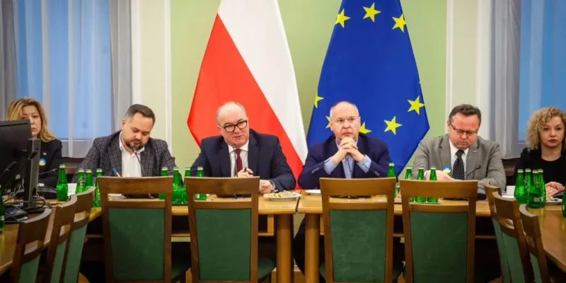 Delegacja PES w Polsce siedzi przy stole konferencyjnym, z flagami Polski i Unii Europejskiej w tle.