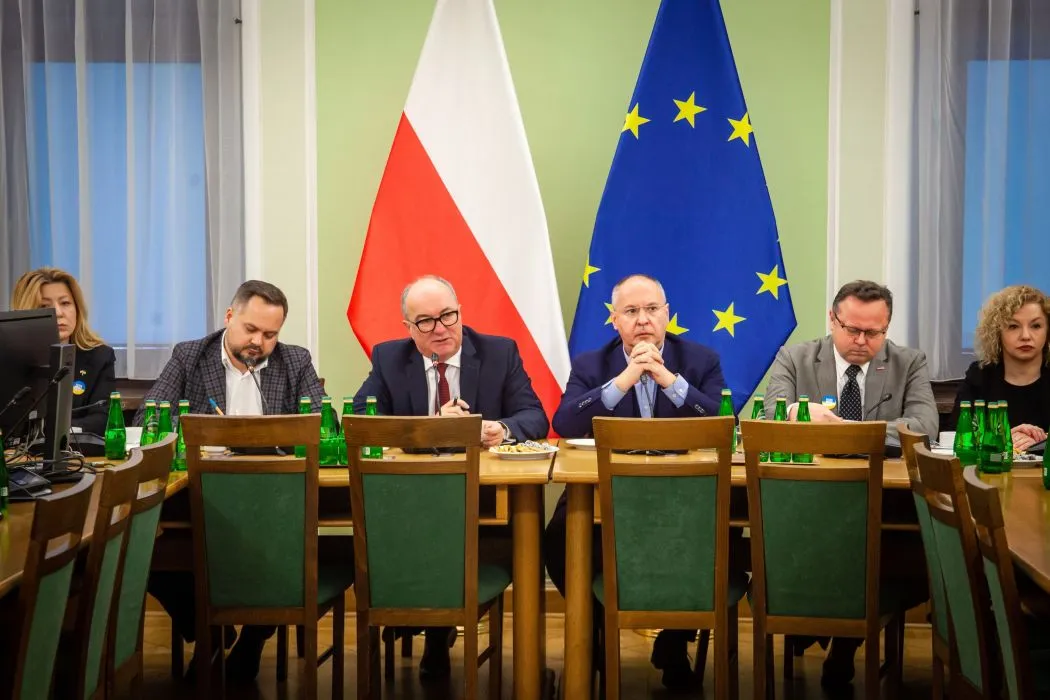 Delegacja PES w Polsce siedzi przy stole konferencyjnym, z flagami Polski i Unii Europejskiej w tle.