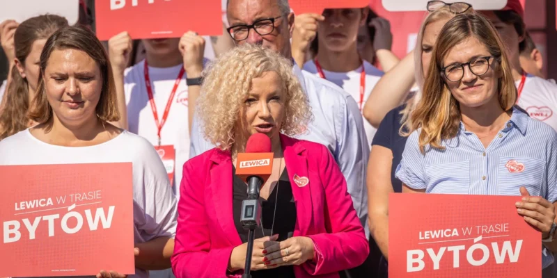 Grupa działaczy Lewicy na wiecu w Bytowie, na pierwszym planie kobieta w różowej marynarce mówiąca do mikrofonu, trzymająca plakat z napisem Bytów.