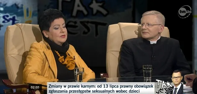 Dwie osoby siedzą w studio programu publicystycznego — kobieta w żółtej kurtce i mężczyzna w sutannie rozmawiają na temat ukrywania przypadków pedofilii wśród duchownych.