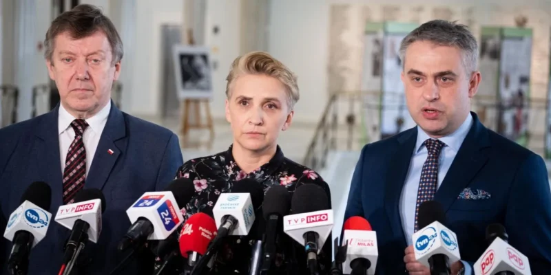 Na zdjęciu trójka polityków udziela wywiadu przed mikrofonami w formalnym otoczeniu.