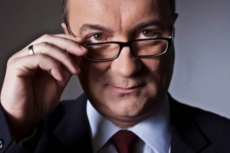 Zbliżenie na mężczyznę w garniturze i krawacie poprawiającego okulary i patrzącego w obiektyw podczas rozmowy.