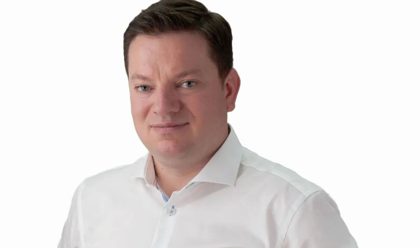 Portret mężczyzny w białej koszuli na białym tle, z lekkim uśmiechem.