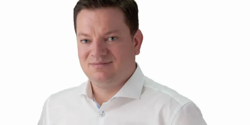 Portret mężczyzny w białej koszuli na białym tle, z lekkim uśmiechem.