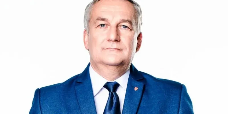 Portret mężczyzny w niebieskim garniturze i granatowym krawacie na białym tle.