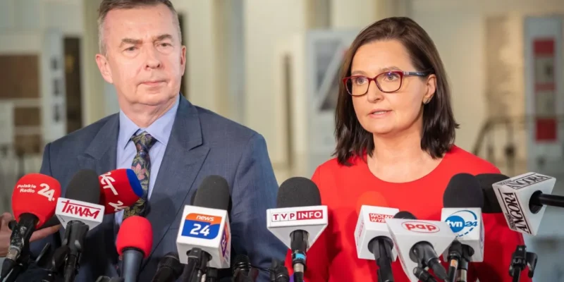 Na zdjęciu widoczni są dwaj mówcy podczas konferencji prasowej, przed którymi ustawione są mikrofony z logo różnych mediów.