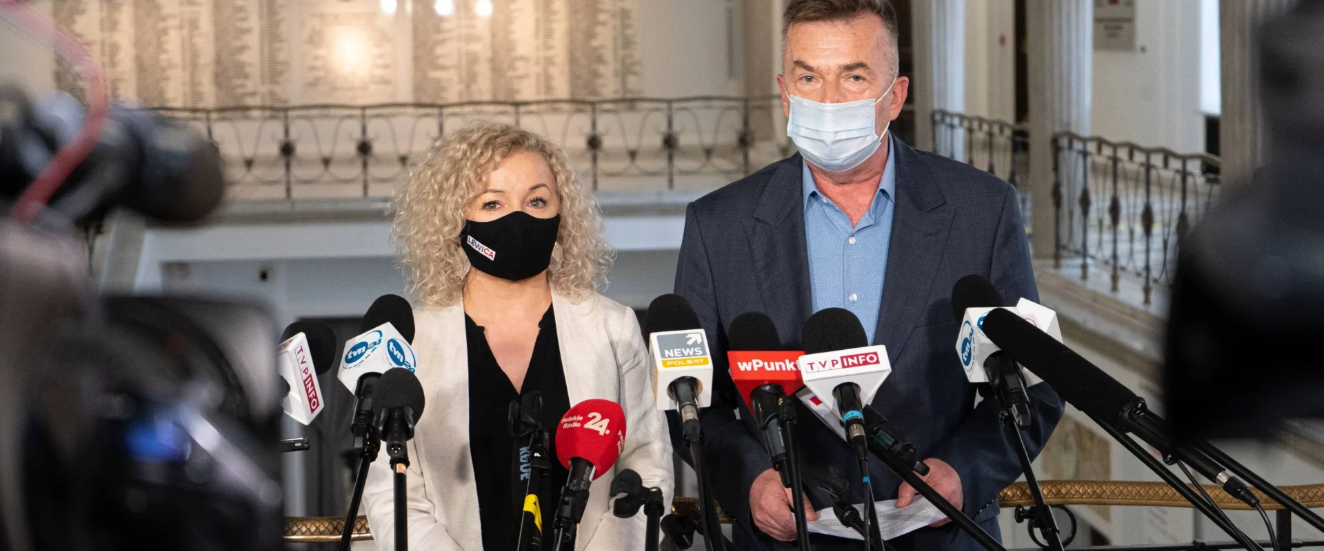 Dwoje przedstawicieli w maseczkach stoi za licznymi mikrofonami podczas konferencji prasowej w budynku PGE GiEK.