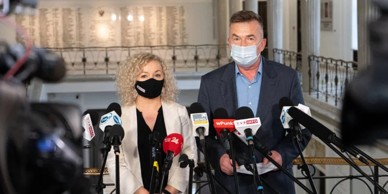 Dwoje przedstawicieli w maseczkach stoi za licznymi mikrofonami podczas konferencji prasowej w budynku PGE GiEK.