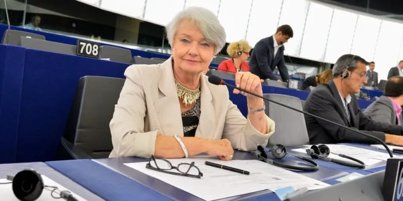 Kobieta siedzi przy stanowisku w sali plenarnej Parlamentu Europejskiego, trzyma mikrofon i spogląda w obiektyw.