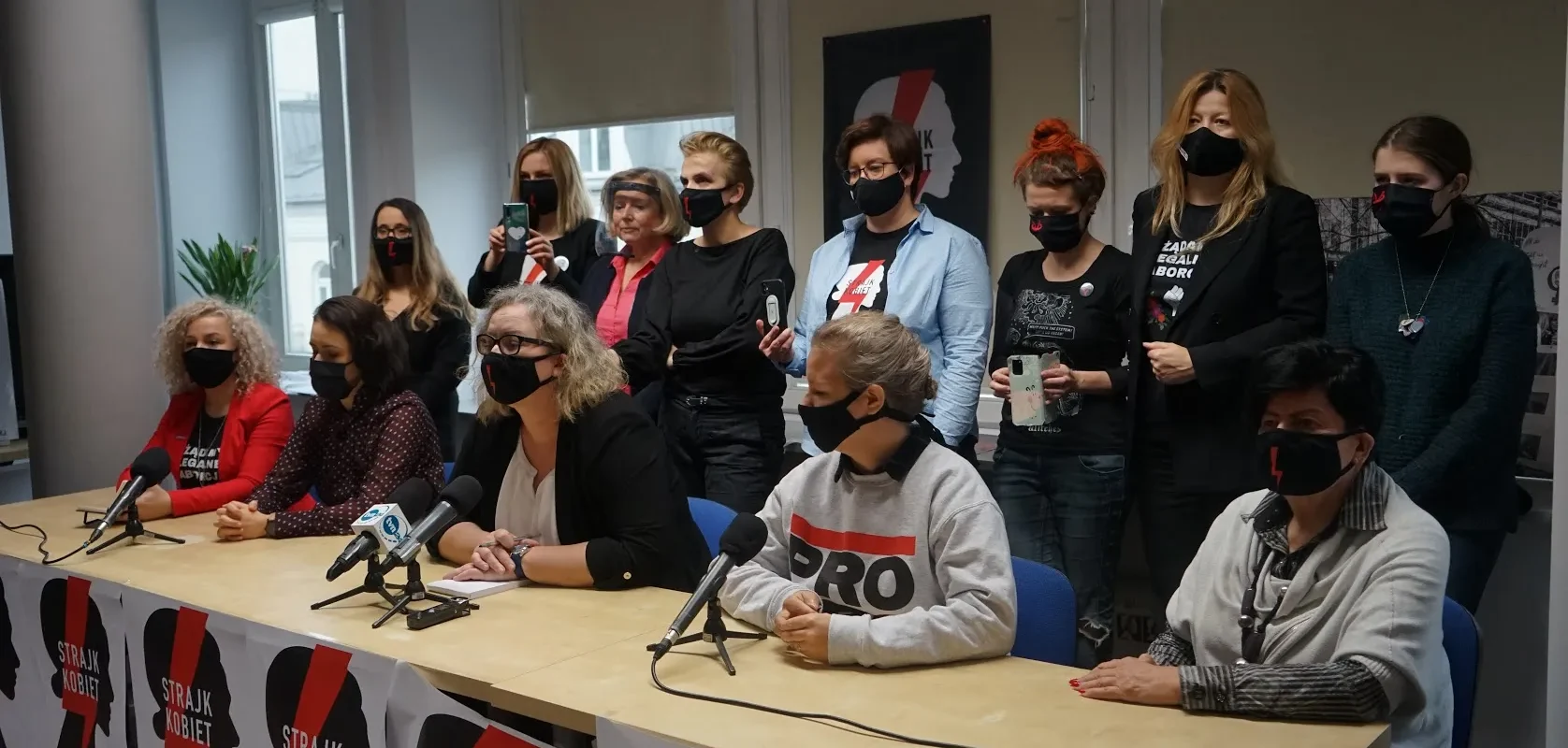 Konferencja prasowa Komitetu Inicjatywy Ustawodawczej dotycząca liberalizacji prawa aborcyjnego, edukacji seksualnej i dostępu do antykoncepcji; przy stole z mikrofonami siedzą prowadzący, a za nimi stoi grupa aktywistek i aktywistów w maseczkach, z banerami Strajk Kobiet w tle.