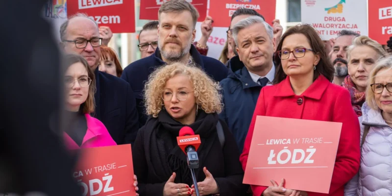 Grupa zwolenników Lewicy na wiecu w Łodzi trzyma plakaty z napisami LEWICA i ŁÓDŹ; centralnie przemawia kobieta z okrągłymi okularami do mikrofonu.