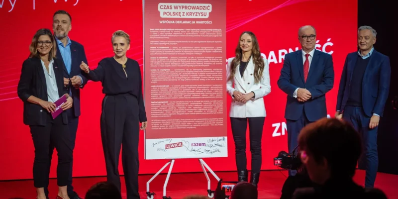 Na zdjęciu widoczna jest grupa polityków podczas wydarzenia promującego deklarację wartości, z czerwonym tłem i dużym plakatem z napisem "Czas wyprowadzić Polskę z kryzysu".