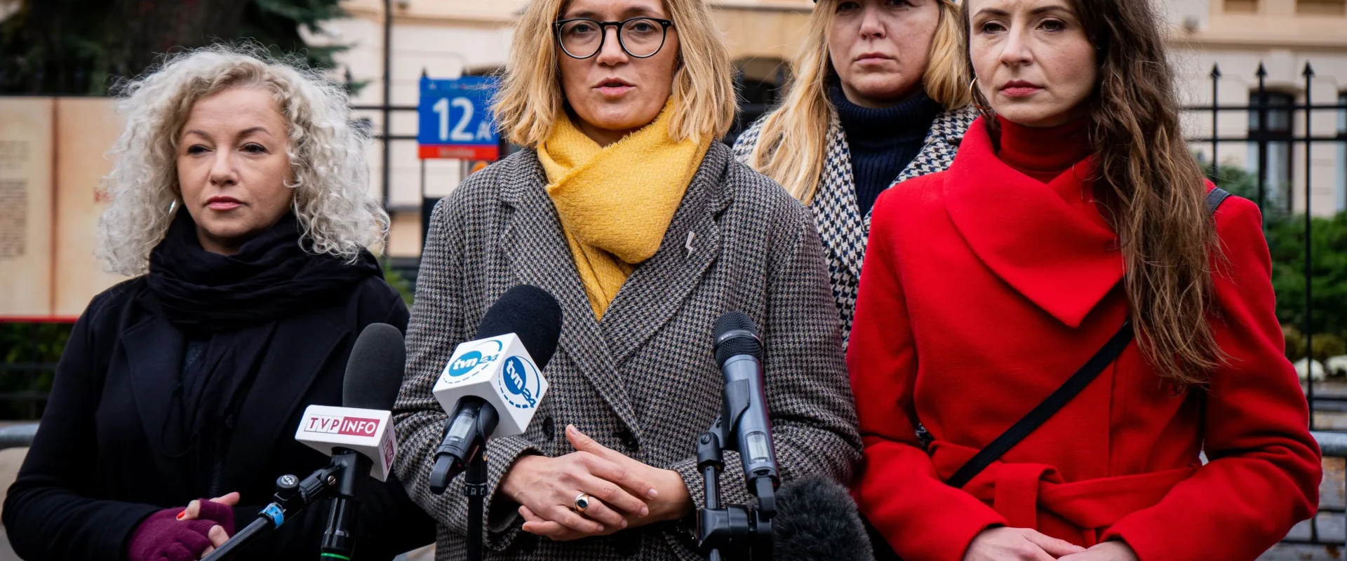 Cztery kobiety stojące przed mikrofonami podczas konferencji prasowej na tle budynku.