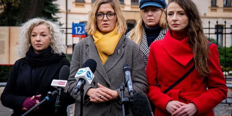 Cztery kobiety stojące przed mikrofonami podczas konferencji prasowej na tle budynku.