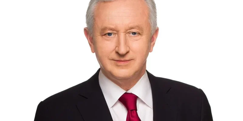 Mężczyzna w czarnym garniturze, białej koszuli i czerwonym krawacie stoi na białym tle.