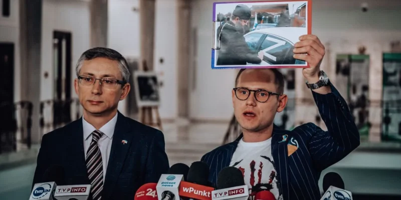 Na zdjęciu dwóch mężczyzn podczas konferencji prasowej, z jednym z nich trzymającym zdjęcie w ręku.