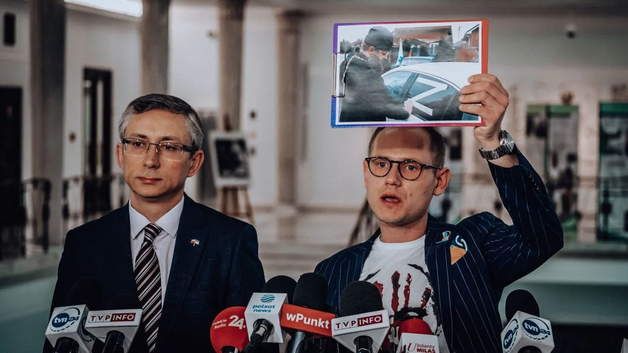 Na zdjęciu dwóch mężczyzn podczas konferencji prasowej, z jednym z nich trzymającym zdjęcie w ręku.