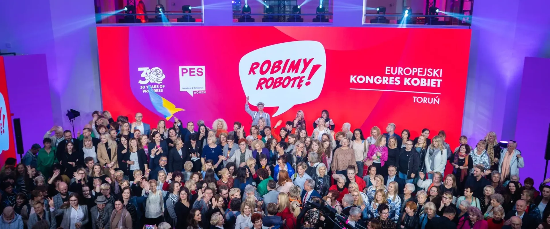 Tłum zgromadzony na Europejskim Kongresie Kobiet w Toruniu, z wieloma osobami pozującymi do zdjęcia przed kolorowym tłem z napisem "Robimy Robotę!".